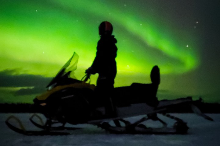 Silhouette on a snowmobile under the green Northern Lights.