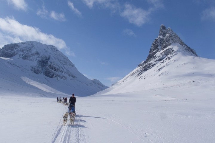 Person dog sledding in snowy mountain landscape with blue sky.