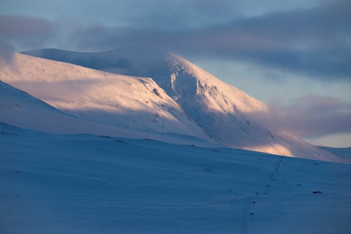 Snow-covered mountain under a cloudy sky with sunlight illuminating the peak.