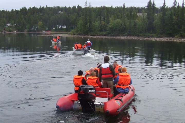 People in orange life vests on red inflatable boats in a forested lake.