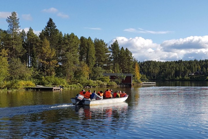 Small boat with people in life jackets on a lake, surrounded by trees under a cloudy sky.