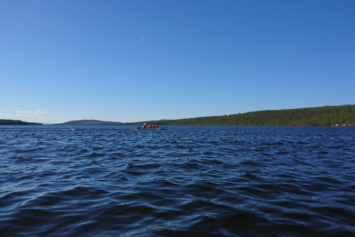 A small boat on a wide lake under a clear blue sky.