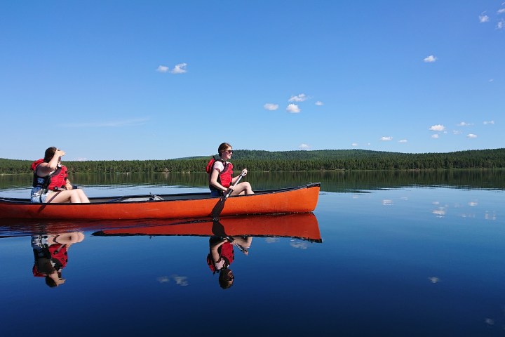 Two people canoeing on a calm lake under a clear blue sky.