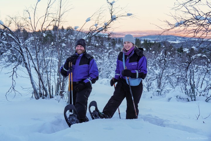 Two people in snowshoes standing in a snowy landscape with trees and sunset.