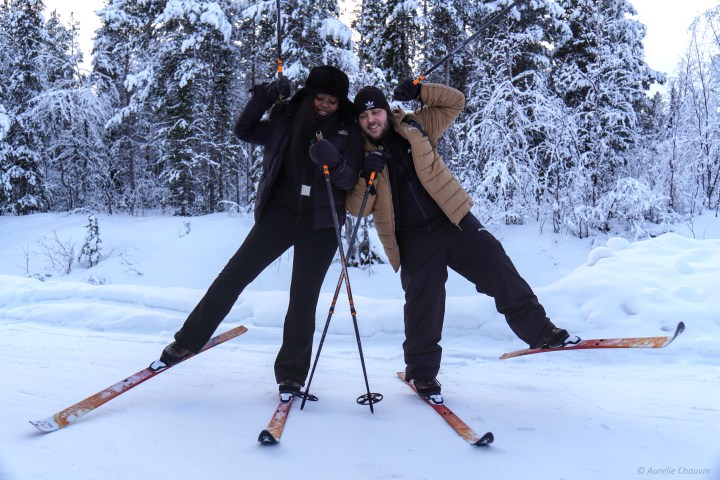 Two people posing on skis with snow-covered trees in the background.