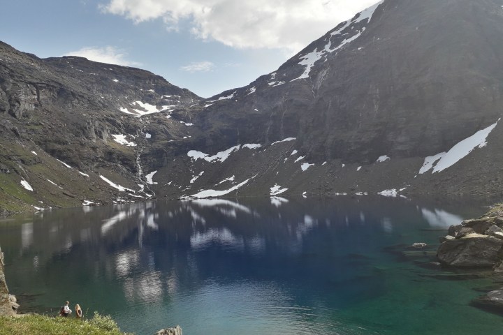 Mountain lake with clear blue water surrounded by snowy peaks and a grassy shoreline.