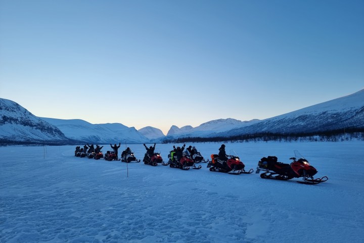 Snowmobiles lined up in snowy mountain landscape at sunrise or sunset.