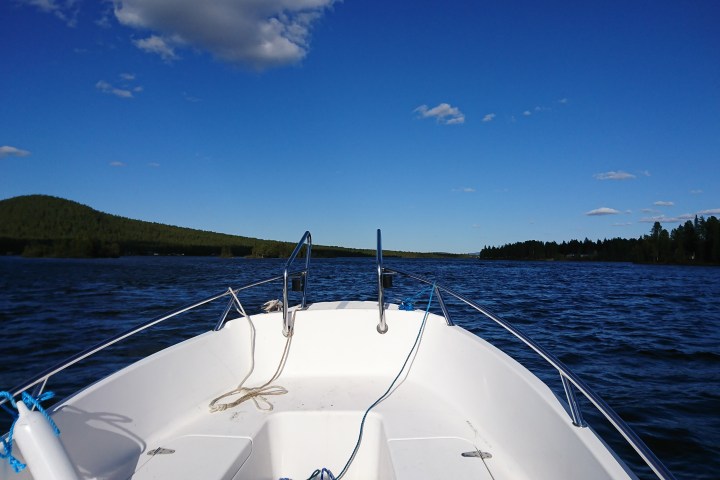 Boat bow navigating a lake with a view of hills and blue sky.