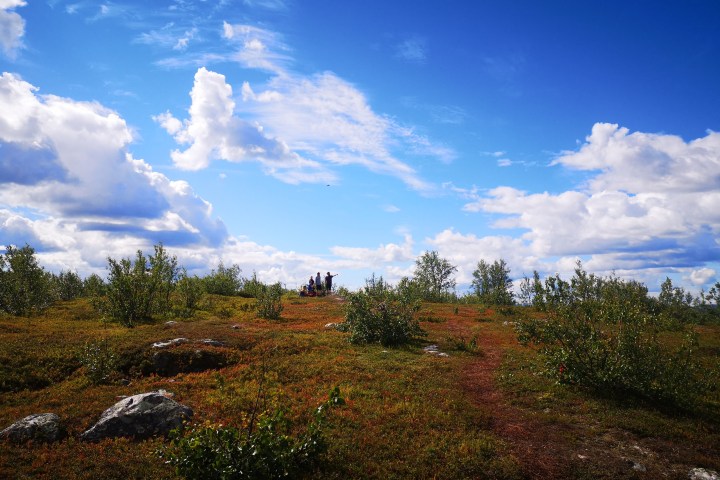 A group of hikers on a grassy hill under a blue sky with scattered clouds.