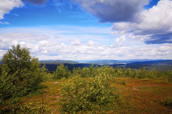 Scenic landscape with green shrubs, distant hills, and a cloudy blue sky.