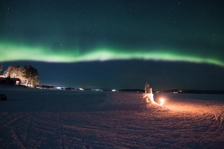 Northern lights over snowy landscape with lit igloo at night.