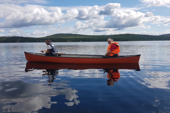 Two people paddling in an orange canoe on a calm lake under a cloudy sky.