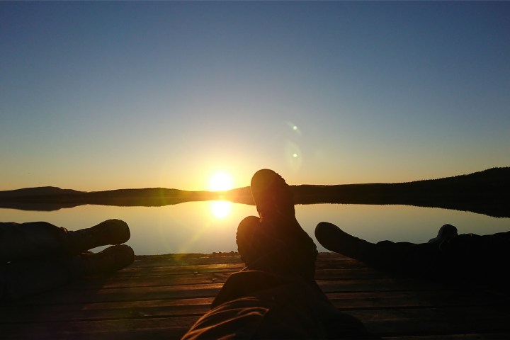 Silhouetted figures lying on a dock at sunset with a calm lake and horizon.
