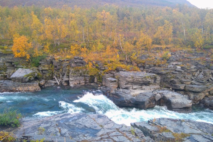River with rapids flowing through rocky landscape and autumn trees.