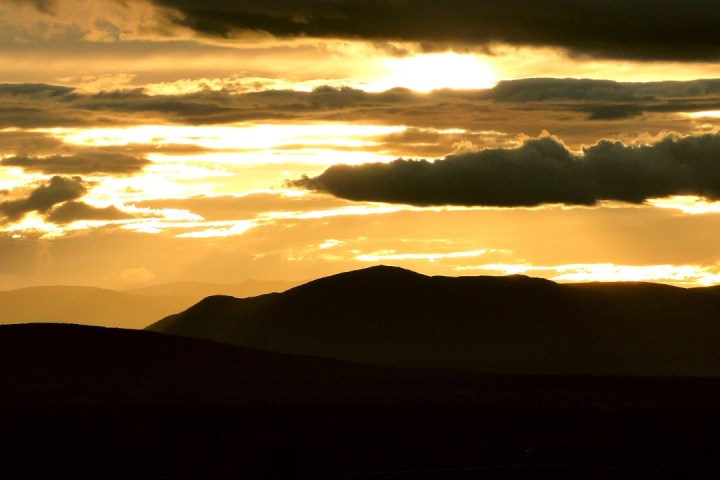 Silhouetted hills under a dramatic cloudy sky during a golden sunset.