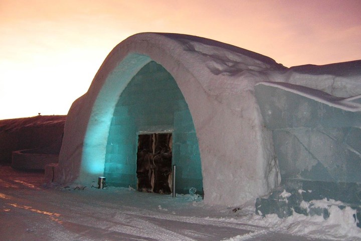 Snow-covered ice building with arch entrance against a sunset sky.