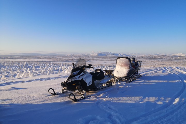 Snowmobile on snowy field with distant snow-covered landscape and clear blue sky.
