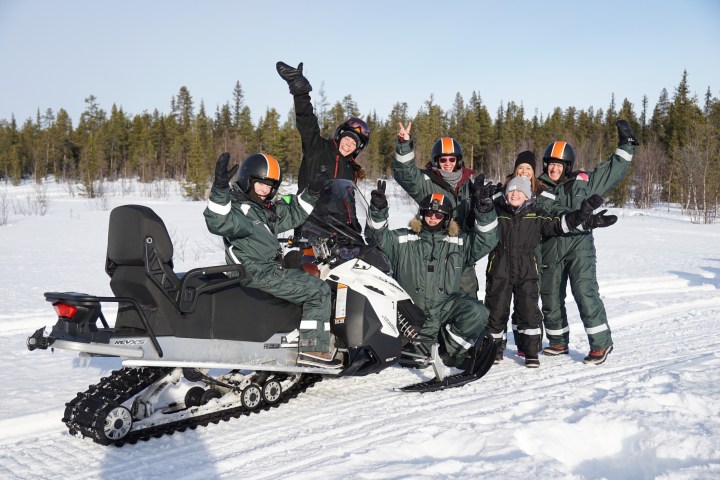 Group of people in snow gear posing with a snowmobile in a snowy landscape.