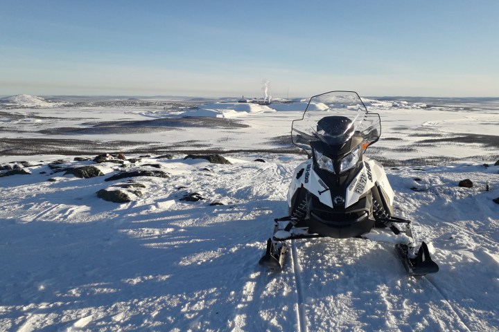 Snowmobile on snowy hilltop overlooking vast icy landscape under clear blue sky.
