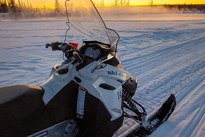 Snowmobile on snowy terrain at sunset with trees in the background.