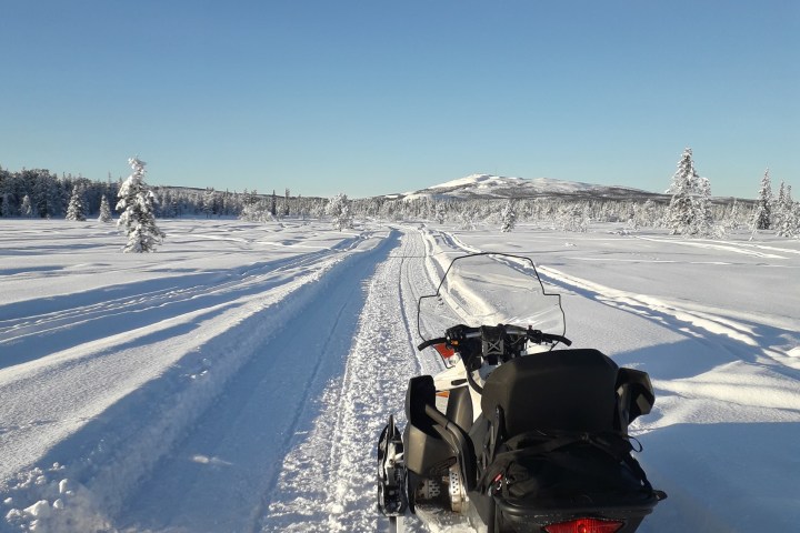 Snowmobile on snowy path with clear blue sky and distant snowy hills