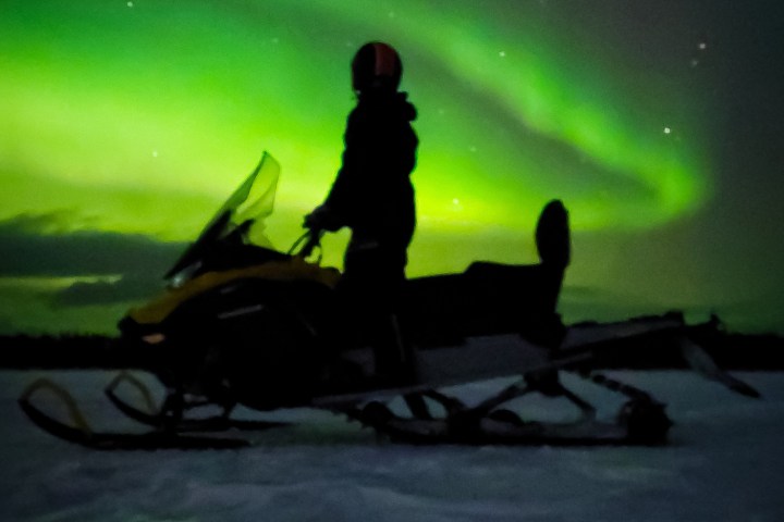 Person on snowmobile under green Northern Lights at night.