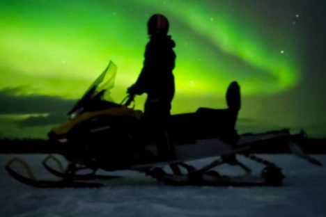 Silhouette of a person on a snowmobile with green aurora borealis in the night sky.