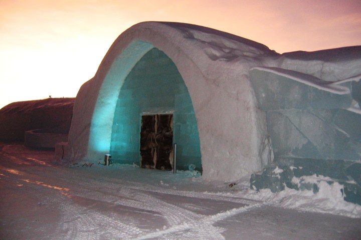 Snow and ice building with arched entrance at sunset, pink sky.