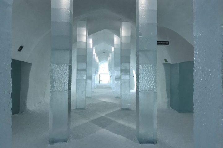Interior of an ice structure with arched ceilings and ice columns lining a long corridor.