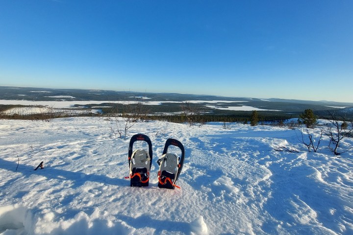 Two snowshoes on a snowy hill under clear blue sky with distant forests