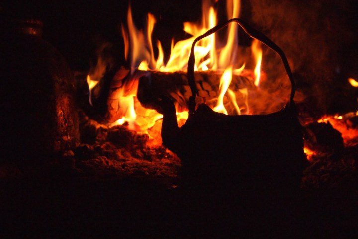 Silhouette of a kettle by a campfire with bright flames.