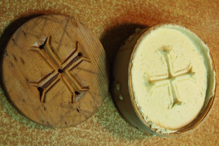 Wooden mold and formed cheese with cross pattern on a wooden surface.
