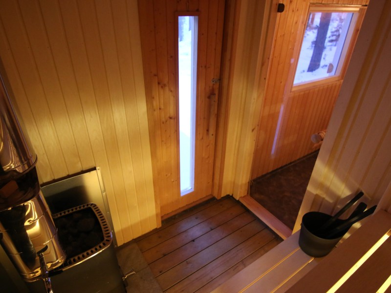 Interior of a wooden sauna with a stove and bucket inside.