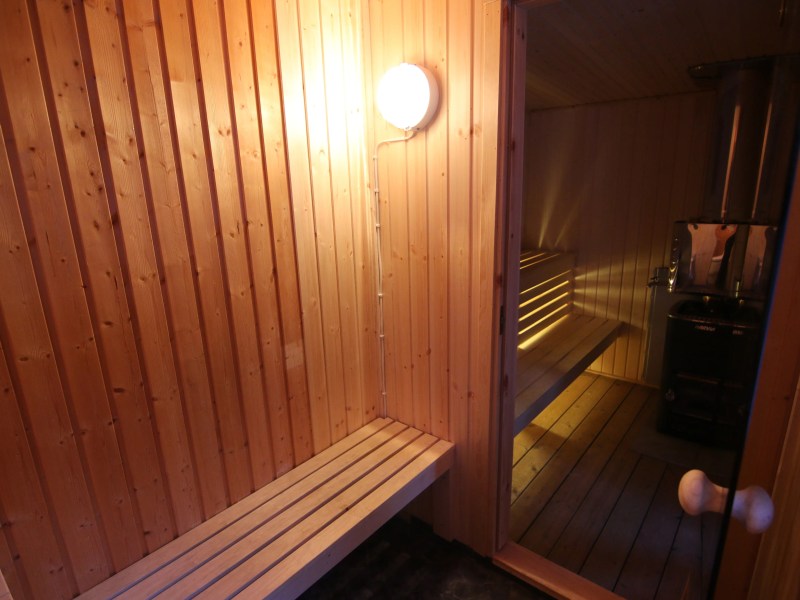 Wooden sauna with benches, a door, and a lit lamp on the wall.