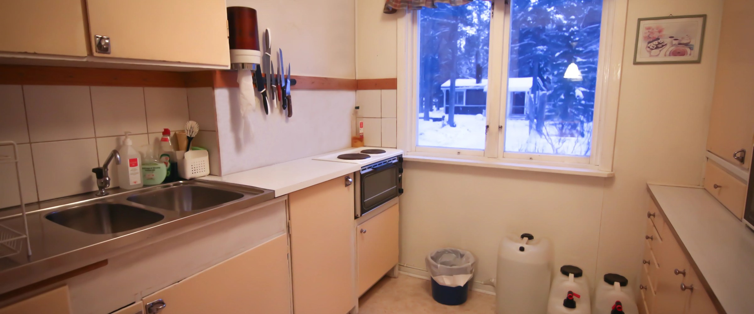 Cozy kitchen with cream cabinets, large window, and knife rack on wall, showing snowy scene outside.