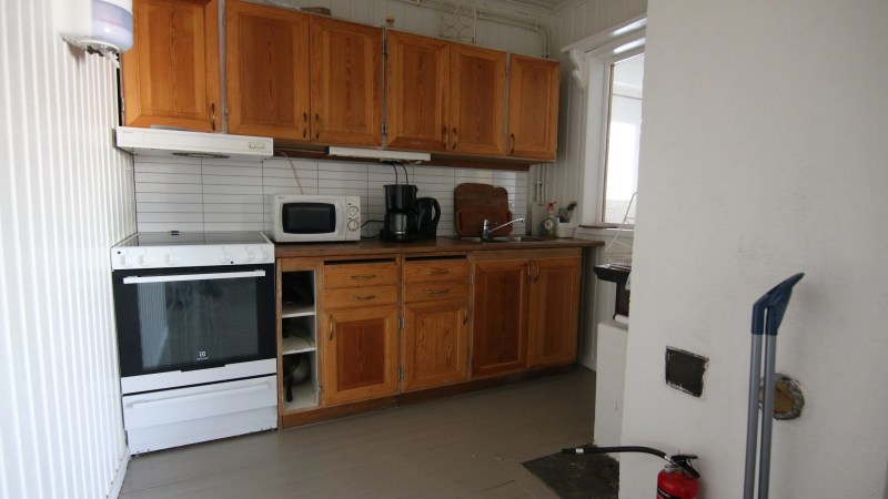 Small kitchen with wooden cabinets, stove, microwave, coffee maker, and fire extinguisher on the floor.