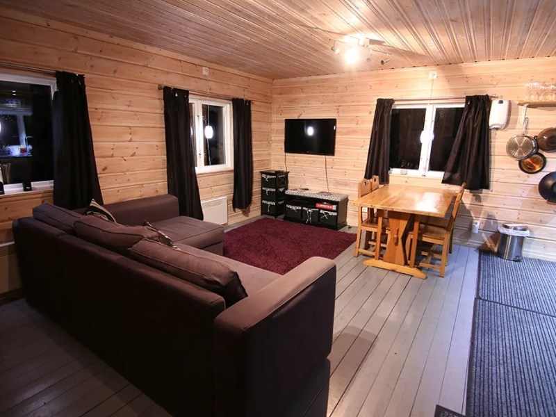 Cozy living room with wood paneling, sofa, dining table, and TV on wall, adorned with dark curtains.