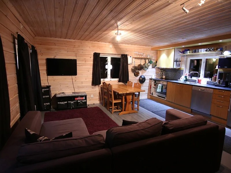 Cozy wooden cabin interior with sofa, dining table, and modern kitchen.