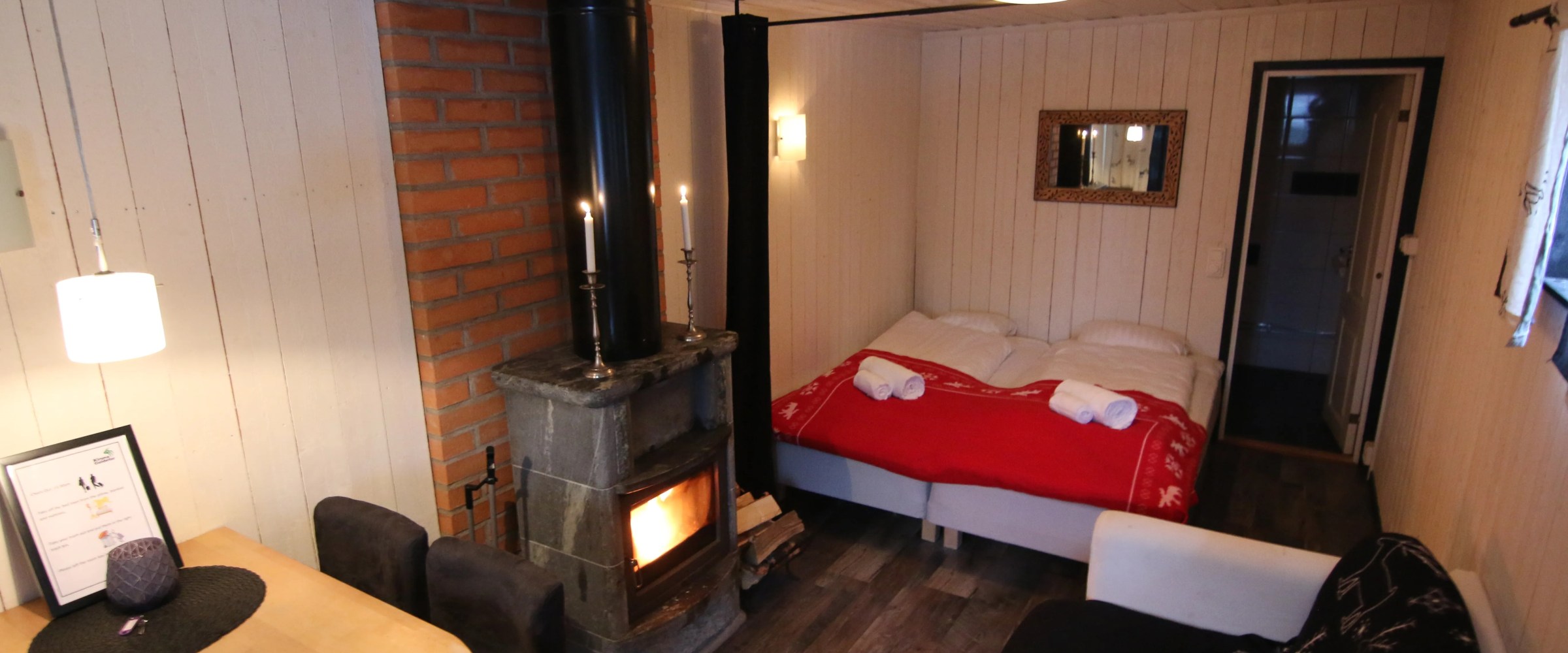 Cozy cabin interior with bed, sofa, wood stove, and dining table.
