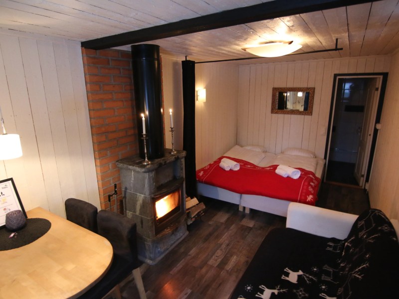 Cozy cabin interior with bed, sofa, wood stove, and dining table.