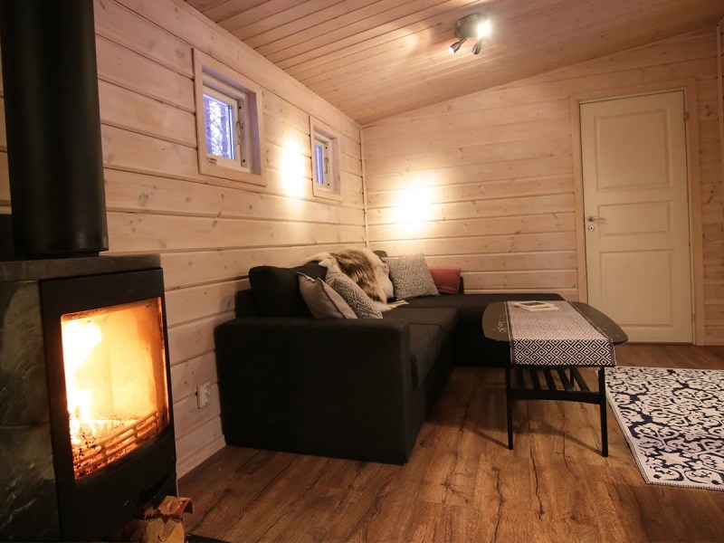 Cozy cabin living room with fireplace, black sofa, patterned rug, and wooden walls.