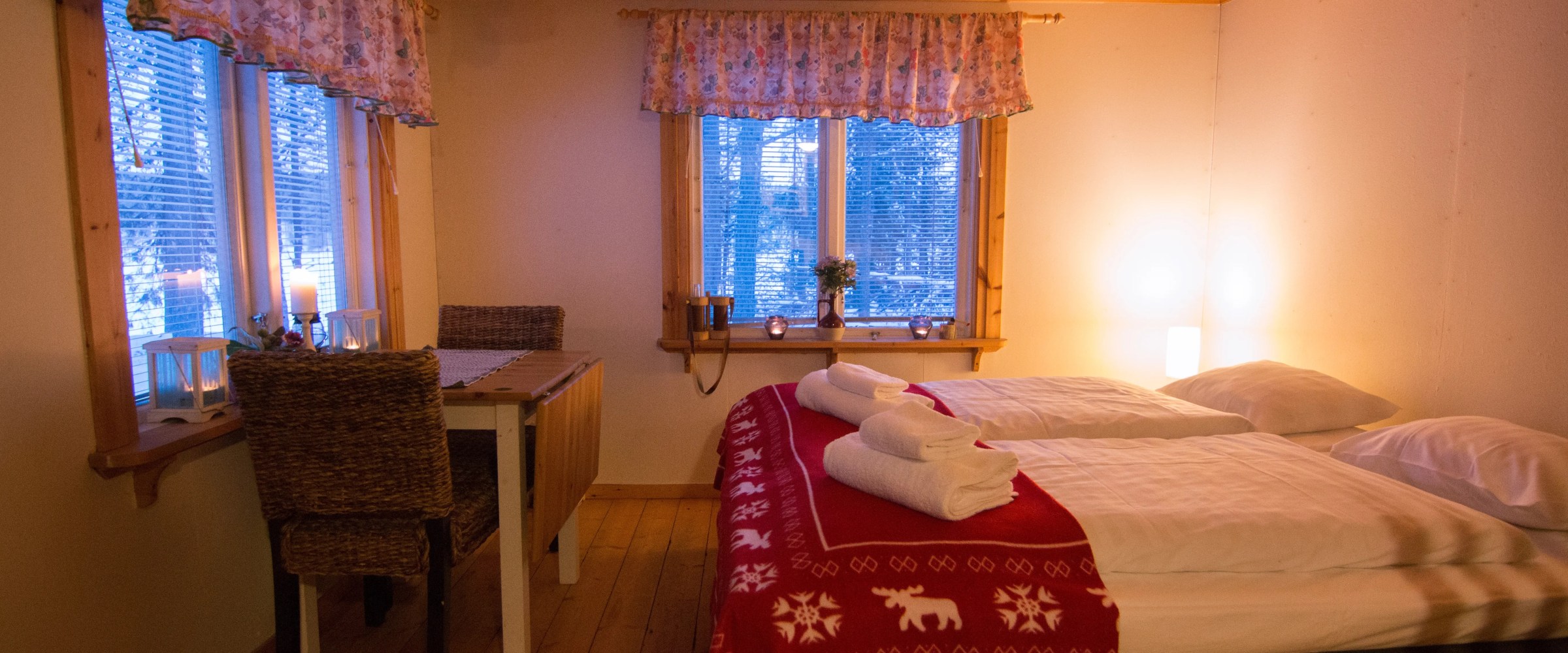 Cozy wooden bedroom with double bed, red blanket, and small dining table near window.