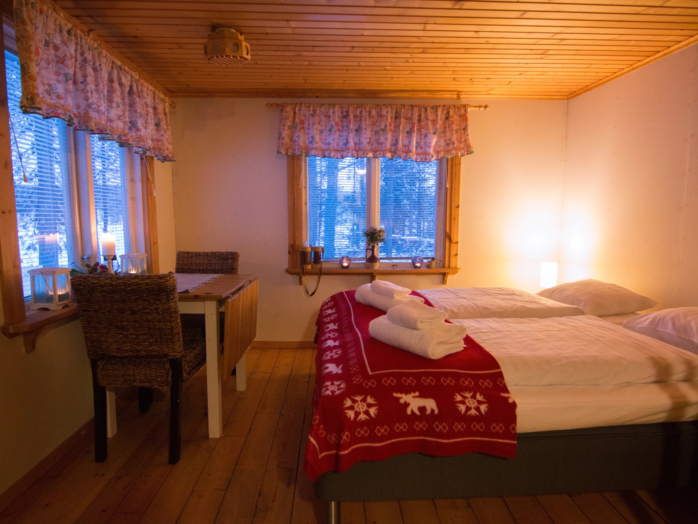 Cozy wooden bedroom with double bed, red blanket, and small dining table near window.