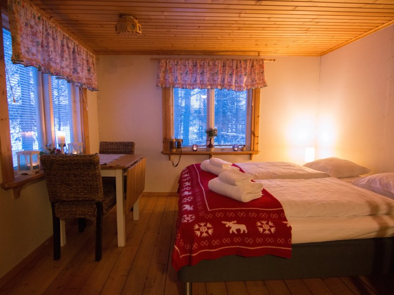 Cozy wooden bedroom with double bed, red blanket, and small dining table near window.