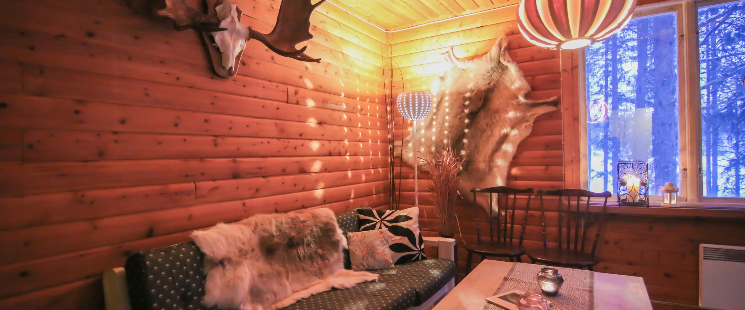 Cozy wood-paneled room with antlers, fur decor, couch, coffee table, and striped pendant light.