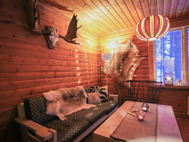 Cozy wood-paneled room with antlers, fur decor, couch, coffee table, and striped pendant light.
