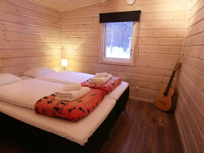 Cozy cabin bedroom with wooden walls, bed, lamp, and guitar.