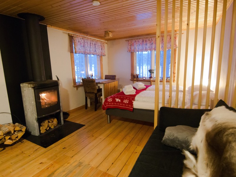 Cozy bedroom with fireplace, wood floors, bed with red blanket, and stacked firewood.