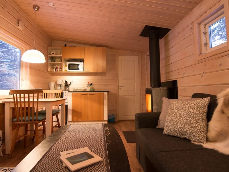Cozy wooden cabin living area with sofa, dining table, small kitchen, and a fireplace.