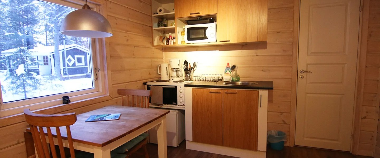Cozy wooden kitchen with dining table, chairs, microwave, and window showing snowy landscape.